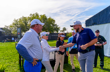 People greet and chat near the 10th hole sign at a golf tournament.