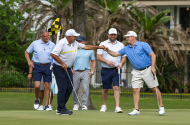 Five golfers fist-bumping and celebrating on the green at The Woodlands Country Club golf course.