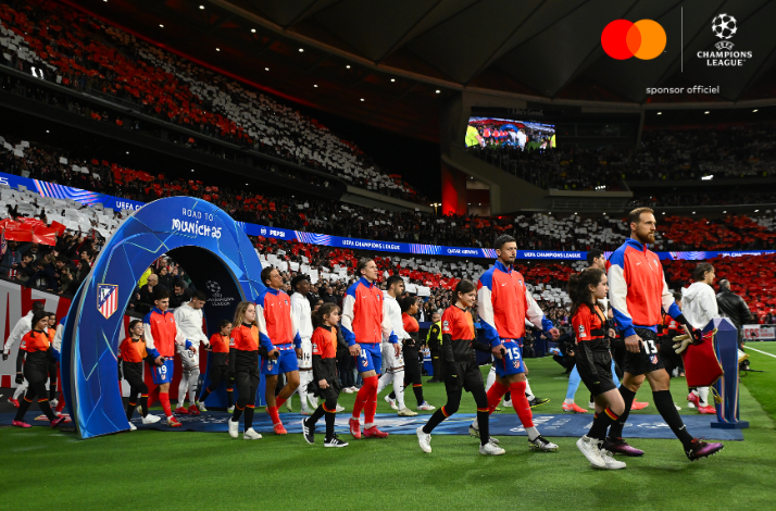 Players and child mascots walking out from the tunnel toward the pitch at UEFA Champions League stadium.