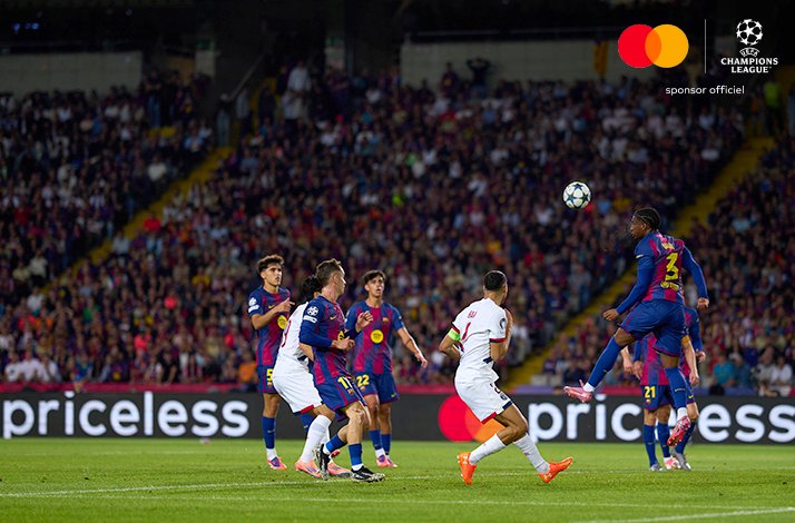 PSG player heading ball under pressure from Barcelona defenders during Champions League league phase match.