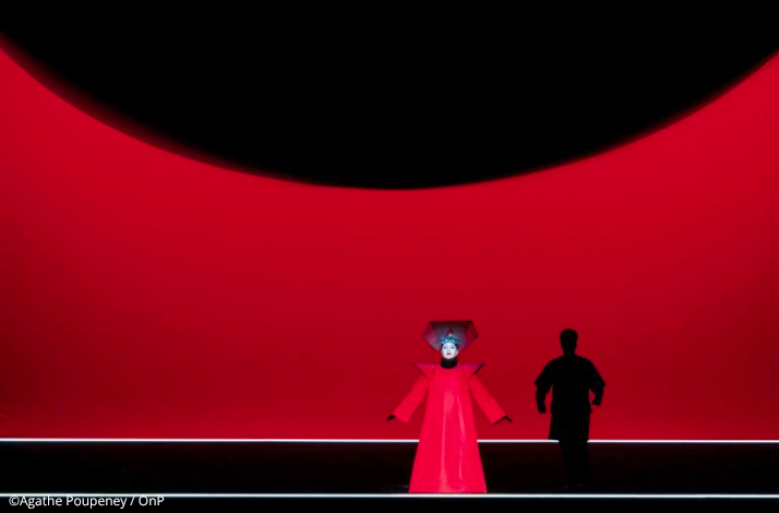 Princess Turandot in a bold red gown under a massive dark eclipse shape at the Opéra Bastille.