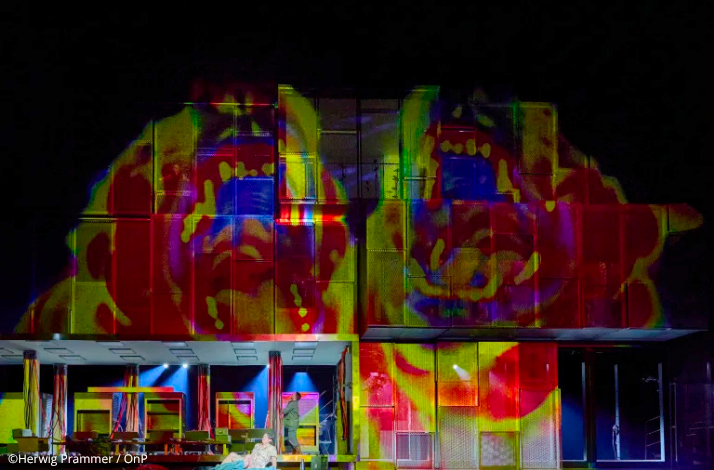 Bold multicoloured projection of an abstract face looming over a darkened stage set during Wagner's The Valkyrie at Opera Bastille.. © Herwig Prammer / OnP.