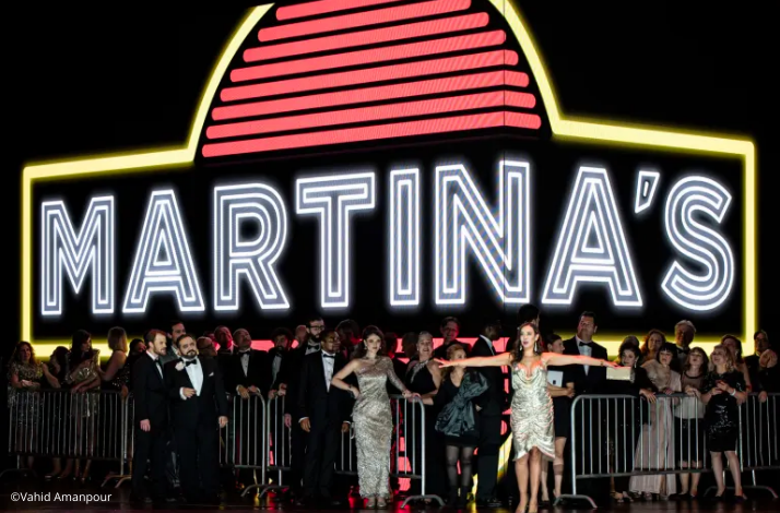 A crowd of performers in formal attire stand in front of a large neon sign reading MARTINA'S. © Vahid Amanpour