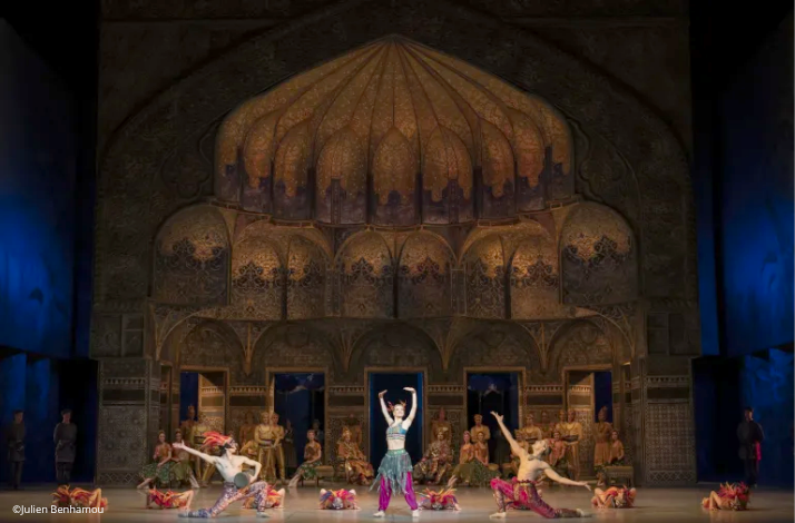 Ballet dancers perform on a grand stage with an intricate, golden dome backdrop during La Bayadère.