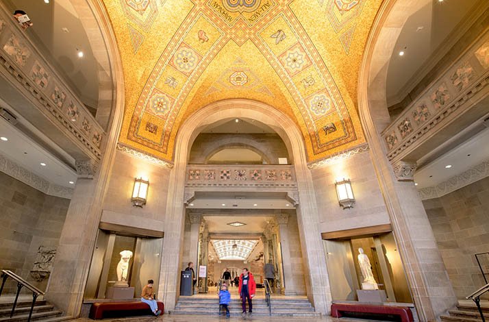 Visitors to ROM walking in the halls of the museum and looking at exhibited sculptures.
