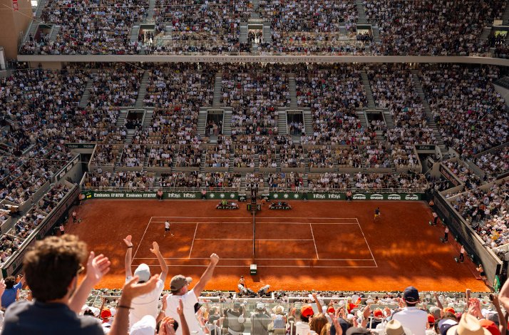 A fan's wide view of a live tennis game in Roland-Garros stadium, filled with fans. 