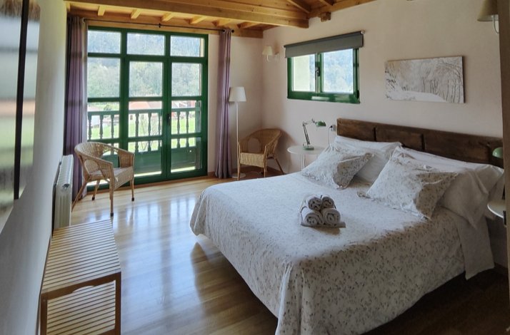 Cozy bedroom with a double bed and green-framed balcony doors overlooking mountains.