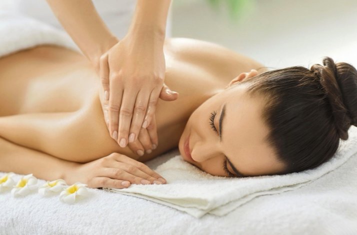 Person lying face down on a towel while a therapist massages their upper back.