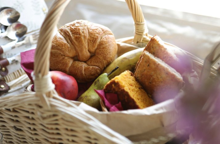 A picnic basket filled with fresh bread, fruit, and baked goods.