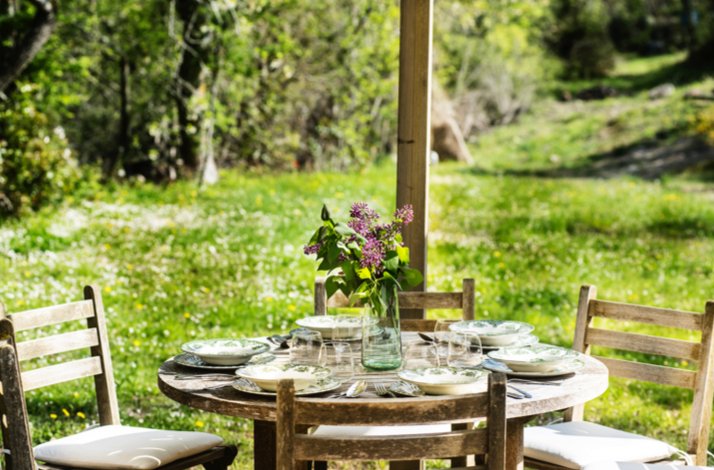 Outdoor wooden dining table with floral decor, surrounded by lush greenery.
