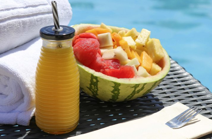 Fresh fruit bowl in a watermelon with juice beside a poolside towel.