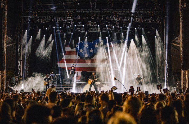 Man playing guitar at country concert in front of large crowd.