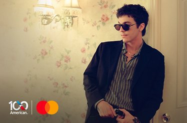 Role Model posing in sunglasses and blazer against floral wallpaper, promoting The Hourglass Tour. Logo of American Airlines and logo of Mastercard. in the lower left corner.
