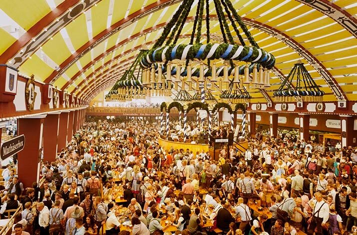 Crowds celebrating inside the Löwenbräu tent at Oktoberfest, with ornate hanging decorations and a central stage.