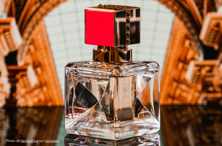 Close-up of a luxury perfume bottle with a red and gold cap, set against an ornate background.