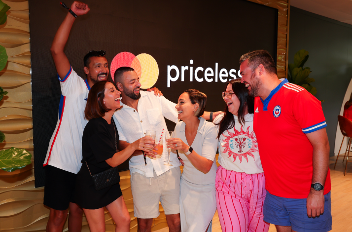 Group celebrates with drinks in front of the Mastercard Priceless lounge sign.