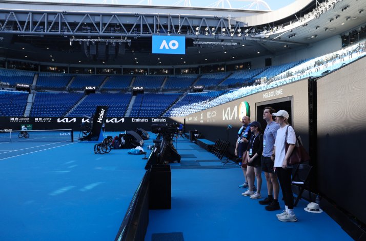 A group of people standing outside the field in an empty Rod Laver Arena, Melbourne.