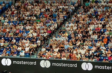 Spectators fill stadium seating above courtside Mastercard advertising boards.