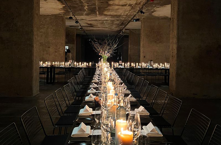 Beautifully set, long table with a dark, intimate ambiance created by numerous candles and low lighting.