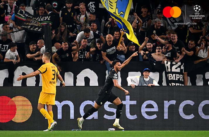 Juventus player gesturing in celebration before a roaring home crowd during Juventus v Borussia Dortmund. Mastercard and UEFA Champions League logos at the top right corner.