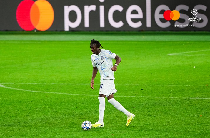 Inter Milan's player in white away kit advancing with the ball at night. Mastercard and UEFA Champions League logos at the top right corner.