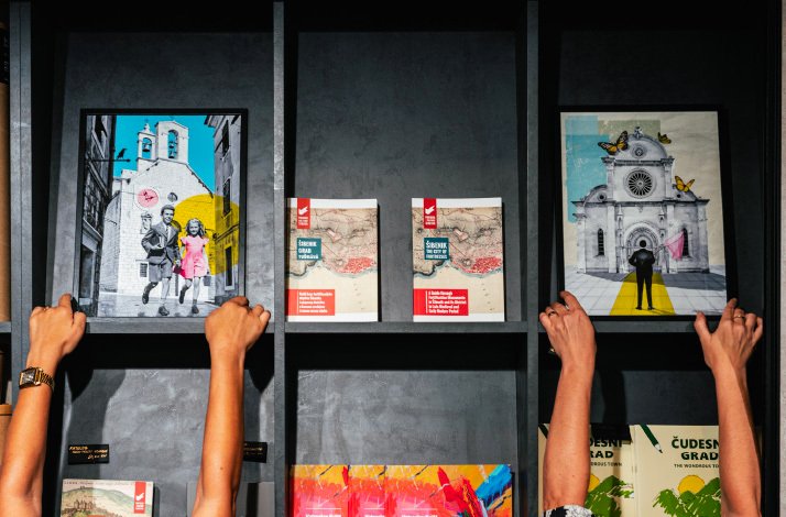A black shelf holding a few paintings and art books in one of the shops at Šibenik fortress.