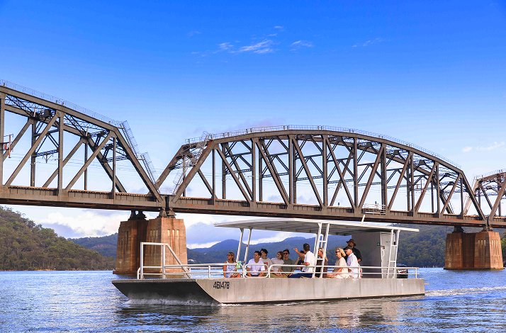 Participants of farm cruise passing by boat on Hawkesbury river below train bridge.