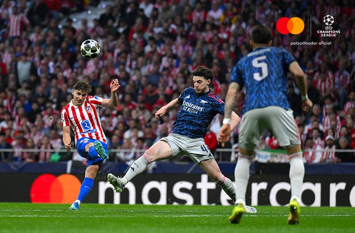 Atletico de Madrid player shooting across Declan Rice of Arsenal during a UEFA Champions League match. Mastercard and UEFA Champions League logos at the top right corner.