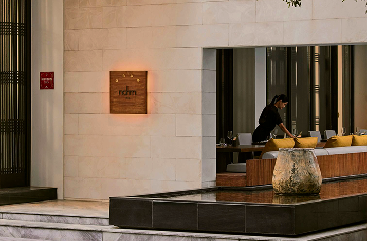 Exterior of Nahm, a Michelin-starred restaurant with a female staff member attending to tables inside.