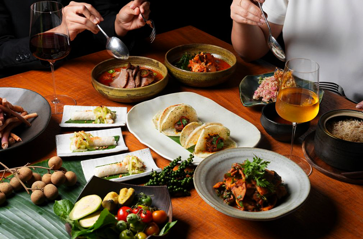 A close-up shot captures an arranged dining scene featuring various dishes, drinks, and two individuals dining.