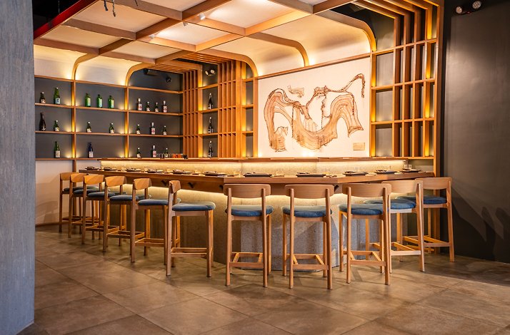 Akiro's chef's counter in Chicago's North River, featuring wooden bar stools, warm lighting, sake shelves, and abstract wall art.