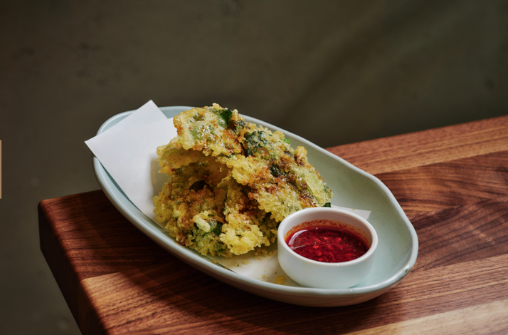 Crispy tempura vegetables served on an oval ceramic dish with a red chili dipping sauce, plated at Uchi West Hollywood.