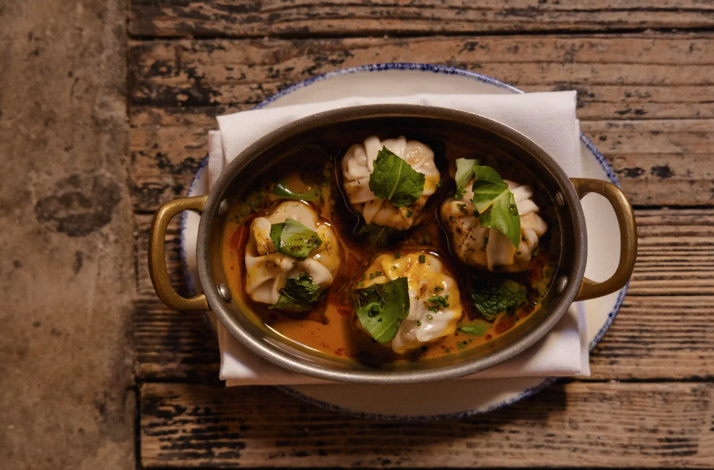 Pleated dumplings garnished with fresh herbs and chives in a rich, spiced broth, reflecting Si! Mon's Panamanian culinary influences.