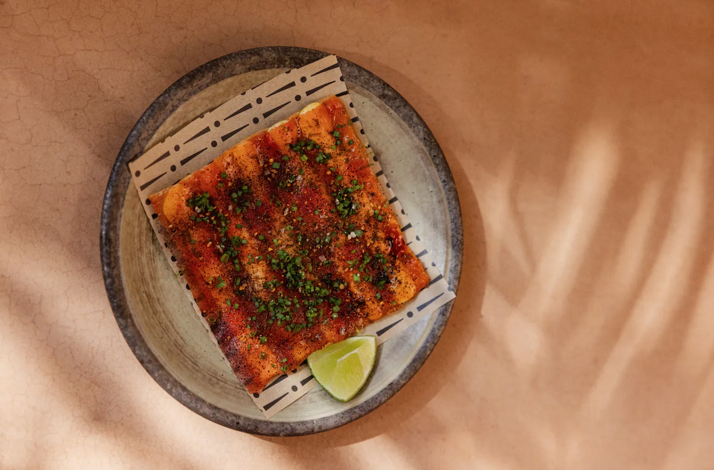 Overhead view of a chili-glazed flatbread garnished with herbs and lime, plated on a decorative bamboo mat at Si! Mon, Venice.