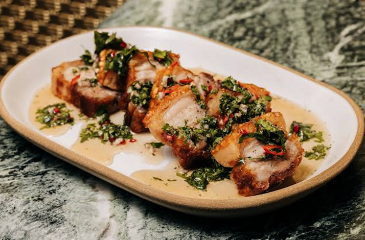 Sliced crispy pork belly topped with herb chimichurri and chili, plated on a ceramic dish at Crying Tiger, Chicago.