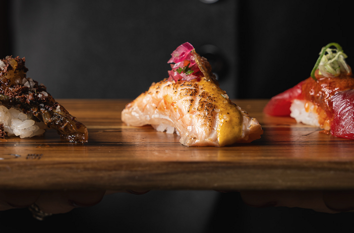 Trio of artfully garnished nigiri at Akiro Chicago, featuring seared salmon and tuna on rice, served on a wooden board.
