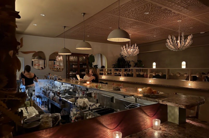 Dimly lit, elegantly appointed bar at Si! Mon restaurant, featuring warm candlelight, ornate chandeliers, and a fully stocked cocktail station.