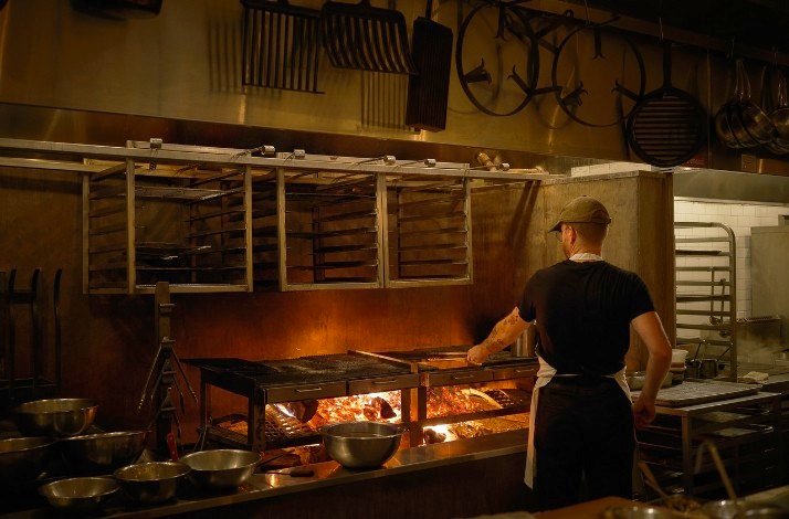 Antico Nuovo's Cook is grilling over an open flame in a rustic, professional kitchen