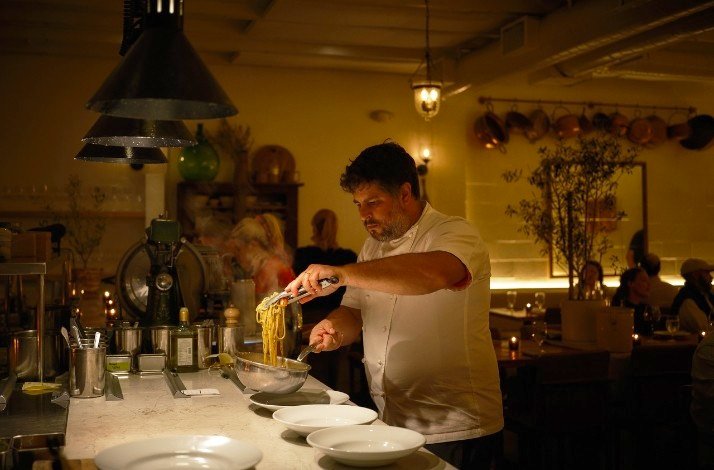 Antico Nuovo's Chef plating pasta in a cozy, warmly lit restaurant kitchen 