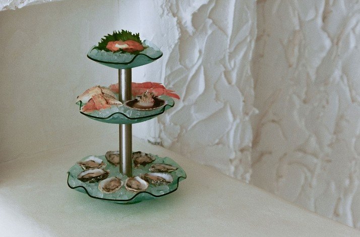Two-tier seafood platter with oysters, crab, and sushi on frosted glass served at CENTO Raw Bar​