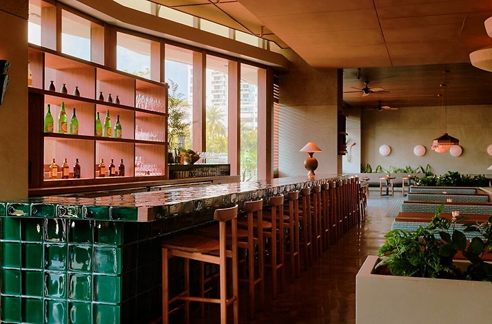 Warmly lit, chic Uchiko Miami dining room featuring a sleek green-tiled bar with wooden stools.
