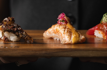 Trio of artfully garnished nigiri at Akiro Chicago, featuring seared salmon and tuna on rice, served on a wooden board.
