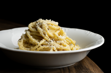 Cacio e pepe pasta mounded in a white bowl, generously topped with grated cheese and cracked black pepper, served at Mother Wolf.