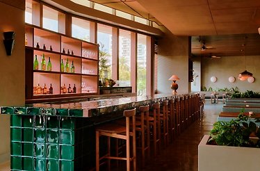 Warmly lit, chic Uchiko Miami dining room featuring a sleek green-tiled bar with wooden stools.