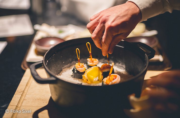 A close-up of a man’s hand inserting canape sticks in canapes cooked at a JRE Restaurant. © Falko Sixel