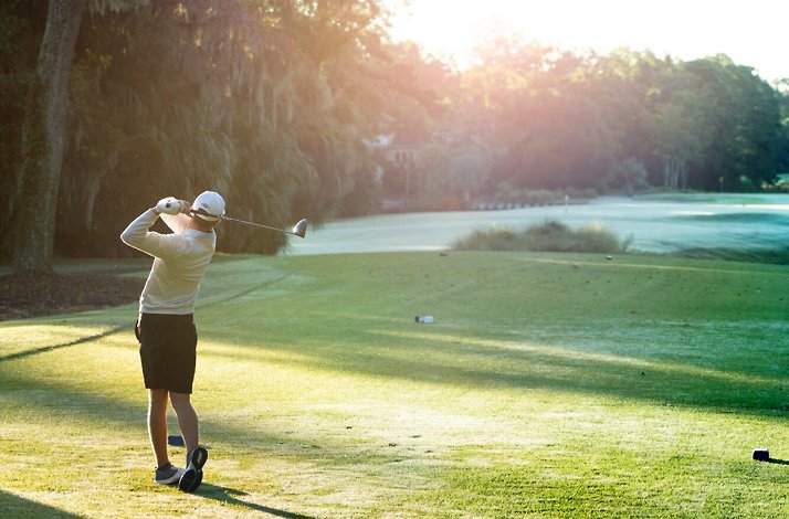 Golfer teeing off at Palmetto Dunes Oceanfront Resort, morning sun.