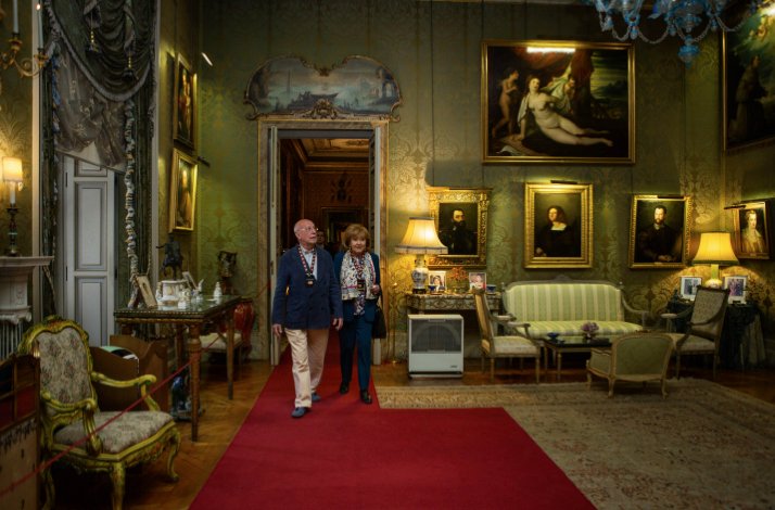 Two visitors walking on a red carpet in an elegant room adorned with classic paintings, antique furniture, and ornate decor at Liria Palace.