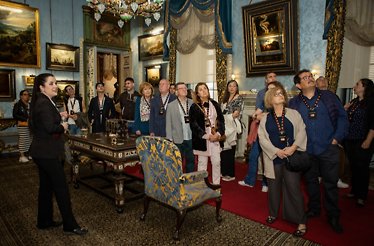 Group of visitors with a guide inside an ornate room at Liria Palace, surrounded by antique furniture, paintings, and chandeliers.