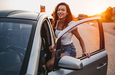 A girl smiling with the door of a car open entering inside of it