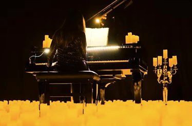 A pianist playing tribute to Ludovico Einaudi in a room full of candles.